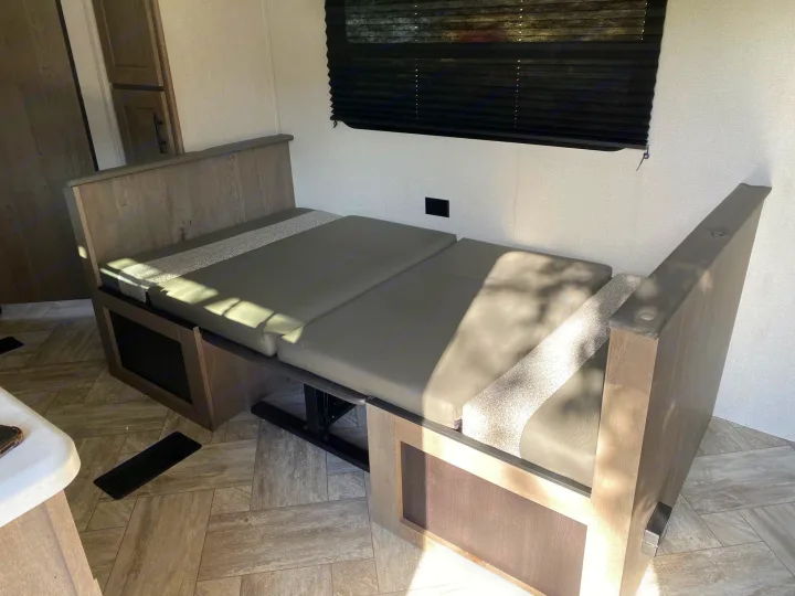 RV rental interior: Wood-toned dinette with gray cushions converted into a bed, bathed in sunlight.. Keystone Springdale 2021