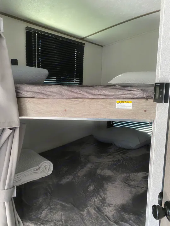 RV rental interior featuring stacked bunk beds with bedding. Upper bunk has light pillow, lower bunk has dark blanket & pillow.. Keystone Springdale 2021