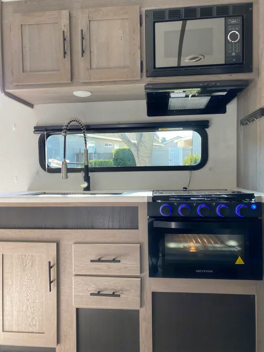 Bright, modern rv rental kitchen featuring microwave, oven, sink, and light wood cabinets.. Keystone Springdale 2021