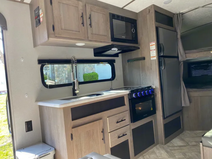 Spacious RV rental interior with a modern kitchen: microwave, stove, fridge, sink, and bunk beds visible.. Keystone Springdale 2021