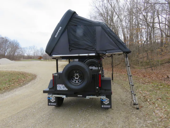 Explore with this robust overland RV rental. Rear view of a black trailer with iKamper rooftop tent deployed & ladder for camping.. Schutt XV-3 Severe Duty 2022