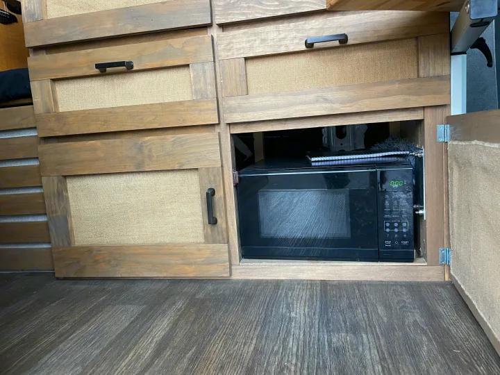 RV rental: Custom wooden cabinetry with burlap inserts and a pull-out microwave, showing efficient camper storage.. Mercedes-Benz Sprinter 2020