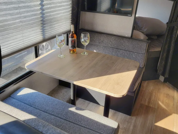 Sunlit RV rental dinette: table, two benches, wine, and a window revealing a Jeep outside.. Forest River Cherokee Grey Wolf 2022