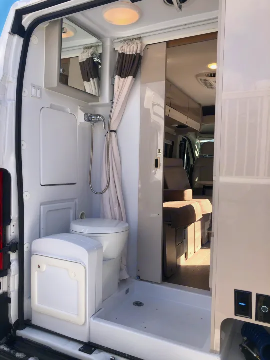 Compact RV rental bathroom with shower, toilet, and mirror, showing efficient use of space in a camper van interior.. Thor Motor Coach Scope 2022