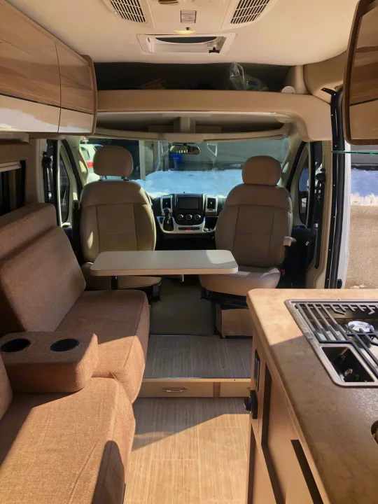 Rv rental interior featuring a front cab, sofa seating with cupholders, and a compact kitchen stove. Ready for adventure!. Thor Motor Coach Scope 2022