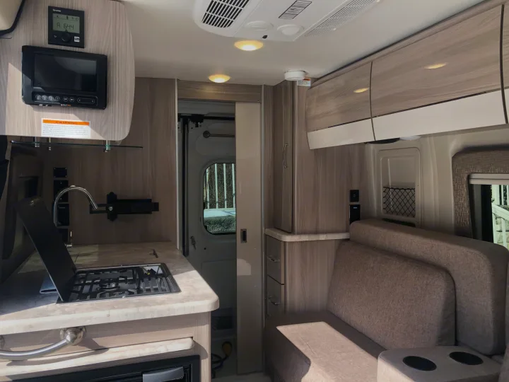 Modern RV rental interior with compact kitchen (stove, sink), comfy seating area with cup holders, and control panels.. Thor Motor Coach Scope 2022