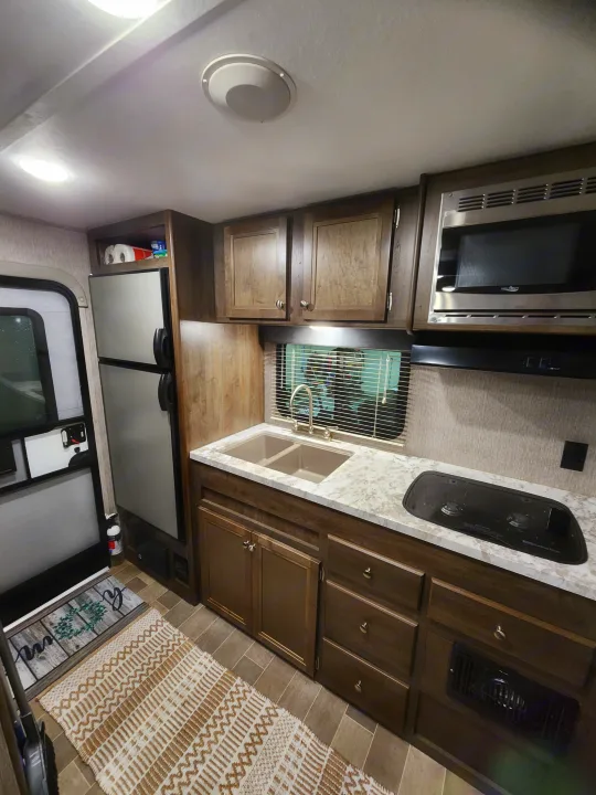 RV rental interior features a compact kitchen with a microwave, sink, cooking area, fridge, and ample cabinets.. Dutchmen Coleman Light LX 2020