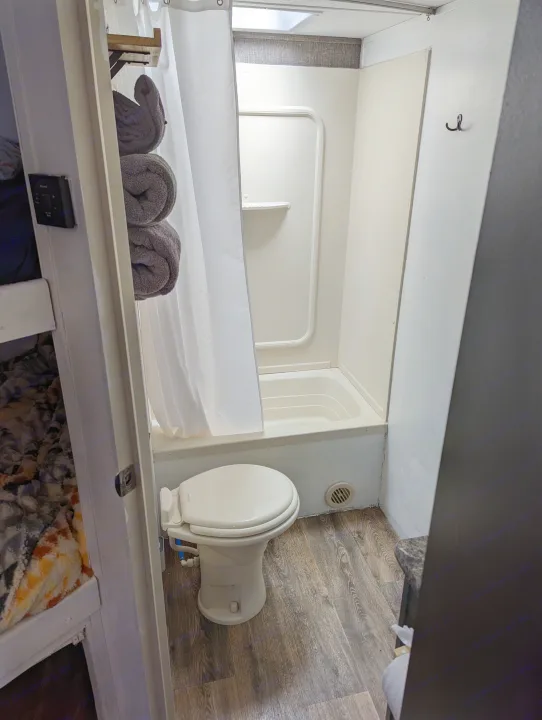 A compact RV rental bathroom: featuring a white shower/tub, toilet, and a peek into the adjacent bunk bed sleeping area.. Keystone RV Springdale Eco-Lite 2016