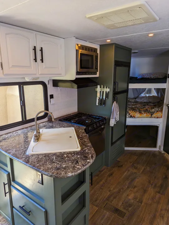 Explore this RV rental's renovated interior, featuring a modern kitchen with green cabinets, white backsplash, & cozy bunk beds.. Keystone RV Springdale Eco-Lite 2016