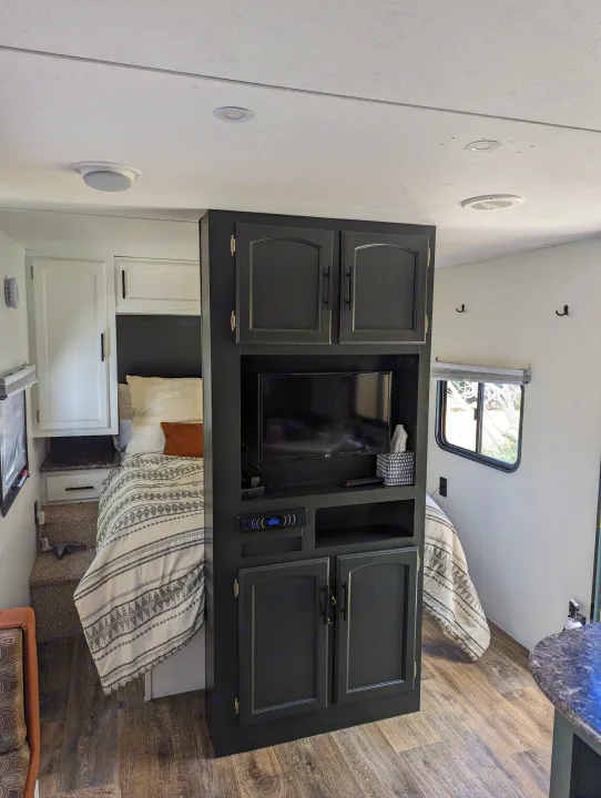 Inside a modern RV rental: a cozy sleeping area with a bed, TV, and black cabinets, featuring wood-look floors.. Keystone RV Springdale Eco-Lite 2016
