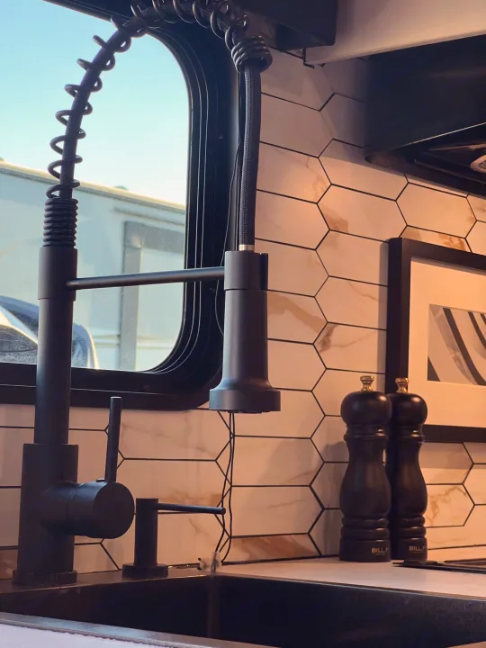 Sleek black faucet, sink, and hexagonal tile backsplash in a modern RV rental kitchen. Another RV is visible outside.. Jayco Featherlight SLX8 2022