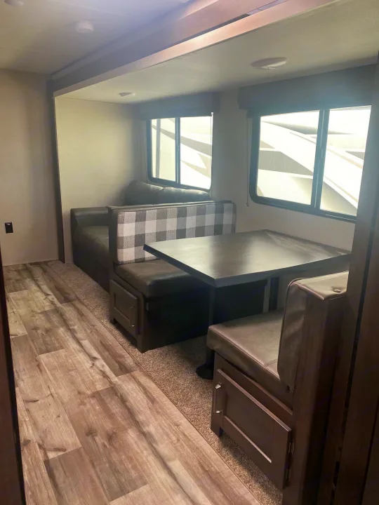This RV rental offers a comfortable dinette with dark upholstered booth seating, a matching table, and large windows.. Grand Design Transcend 2022
