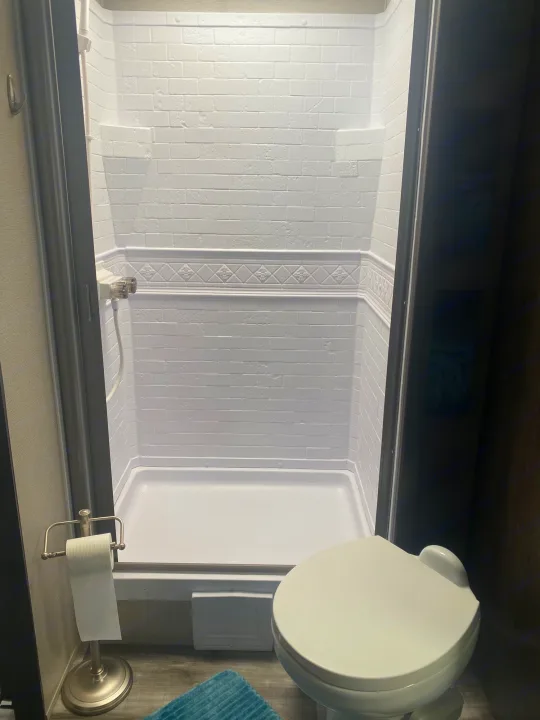 Clean RV rental bathroom showcasing a white shower with decorative trim, a toilet, and freestanding toilet paper holder.. Grand Design Transcend 2022