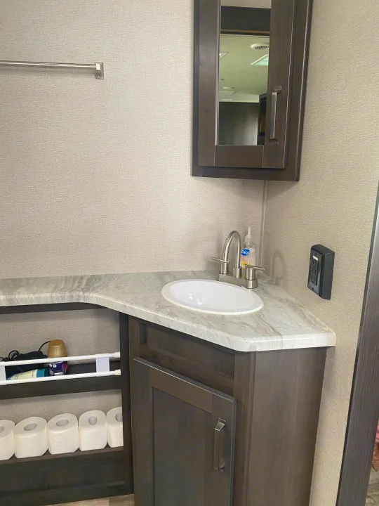 RV rental bathroom featuring a modern corner vanity with sink, mirrored cabinet, and convenient open shelving storage.. Grand Design Transcend 2022