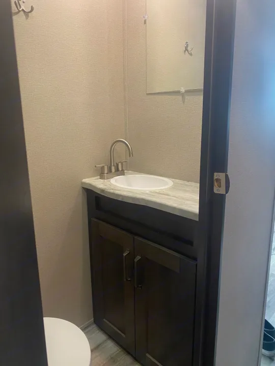 This compact RV rental bathroom features a dark vanity with sink and mirror. A toilet is partially visible on the left.. Grand Design Transcend 2022