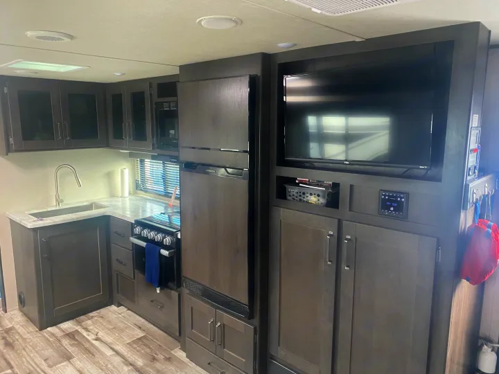 RV rental interior: A modern kitchen with stove, sink, and fridge, adjacent to an entertainment TV area.. Grand Design Transcend 2022