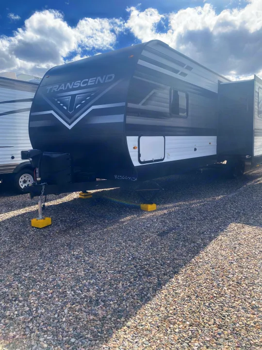 Transcend travel trailer: a spacious black and white RV rental, parked on a gravel lot under blue sky.. Grand Design Transcend 2022
