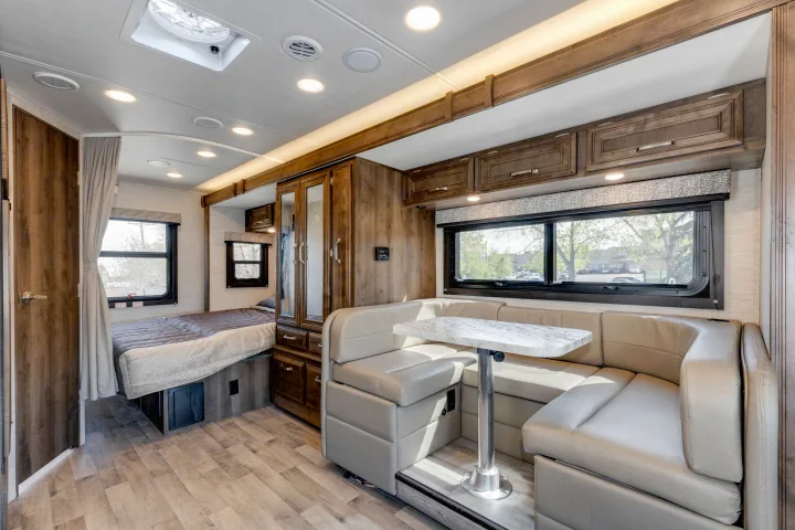 Inside this modern RV rental: a U-shaped dinette, bedroom area with curtain, and wood finishes throughout for travel comfort.. Jayco Melbourne 2022