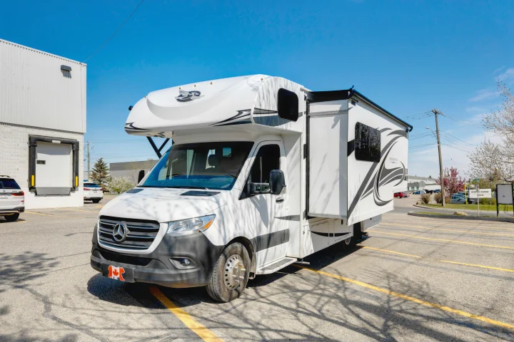 White Jayco Melbourne Class C RV rental on a Mercedes-Benz chassis, parked on a sunny asphalt lot with tree shadows.. Jayco Melbourne 2022