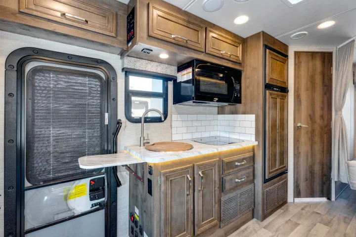 Inside an RV rental: a modern kitchen area with a microwave, sink, and stovetop, adjacent to a unique screened entry door.. Jayco Melbourne 2022