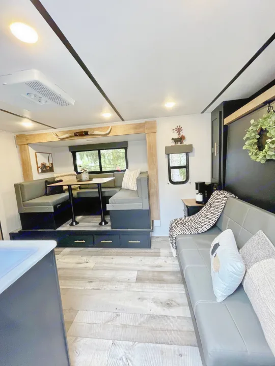 Bright & modern RV rental interior with a U-shaped dining booth, comfy sofa, and rustic charm for your mobile adventures.. Keystone RV Springdale Mini 1810BH 2023