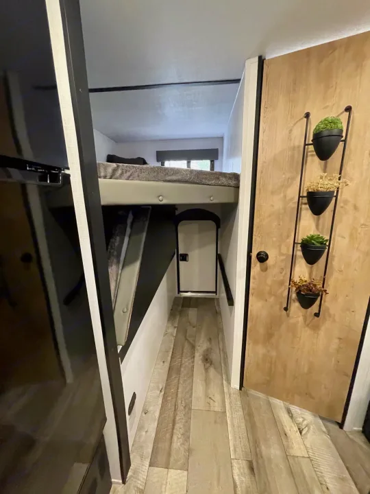 Experience compact comfort in this RV rental's interior, featuring bunk beds, a slim hallway, and a decorative plant display.. Keystone RV Springdale Mini 1810BH 2023