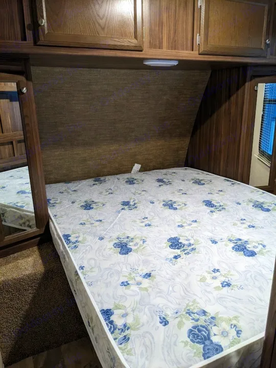 Inside an RV rental: a cozy bedroom with a floral mattress, wood cabinetry, and an integrated mirror. Ready for travel comfort.. Coachmen Apex LE 2018