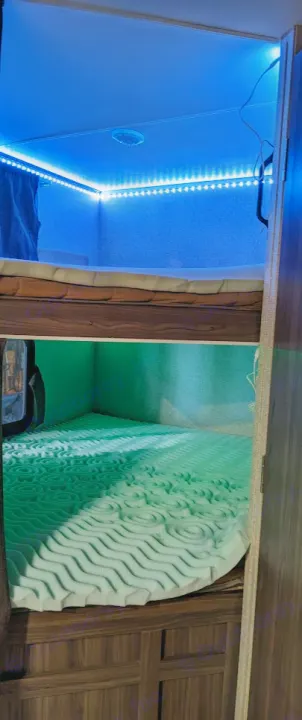 Inside an RV rental: cozy bunk beds. Top bunk has blue LED lighting, bottom features a green-textured foam mattress.. Coachmen Apex LE 2018