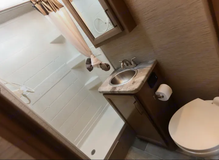 Clean RV rental bathroom featuring a shower, vanity with a stainless steel sink, mirror, and toilet.. Thor Magnitude 2021