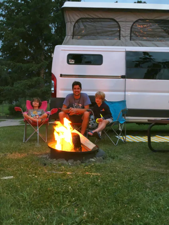 Family enjoying a cozy campfire night at their RV rental campsite, complete with a pop-top camper van.. Dodge Promaster 2017
