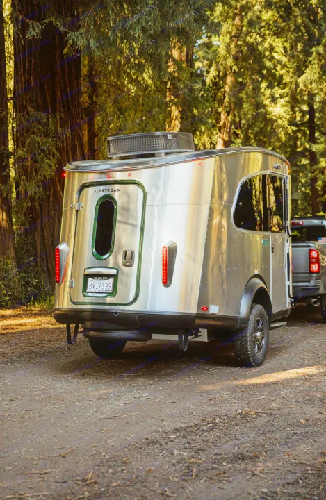 A shiny Airstream travel trailer, perfect for RV rental, is parked among tall redwood trees for an outdoor adventure.. Airstream Other 2023