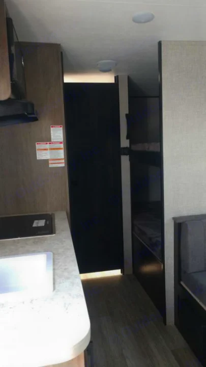 Inside this rv rental: kitchenette with sink, dark door, and bunk beds. Bright interior lighting and wood-look floor.. Jayco Jay Flight SLX 2022