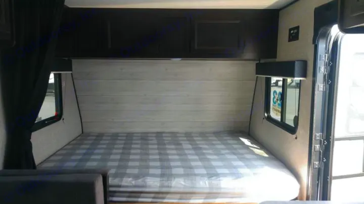 Inside this RV rental, find a comfortable bed with plaid bedding, overhead cabinets, and windows on both sides.. Jayco Jay Flight SLX 2022