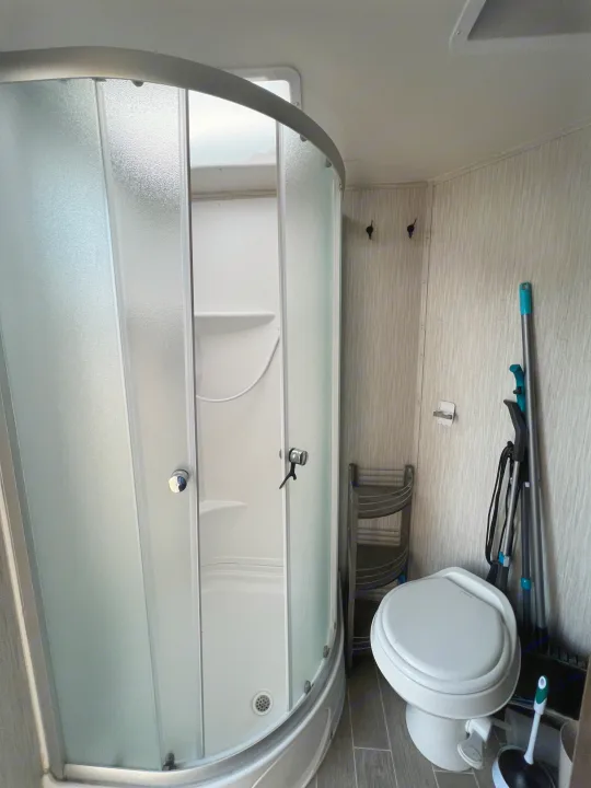 Compact RV rental bathroom showing a curved shower, toilet, and cleaning tools. Efficient use of space for travel.. Forest River Grey Wolf 29te 2021