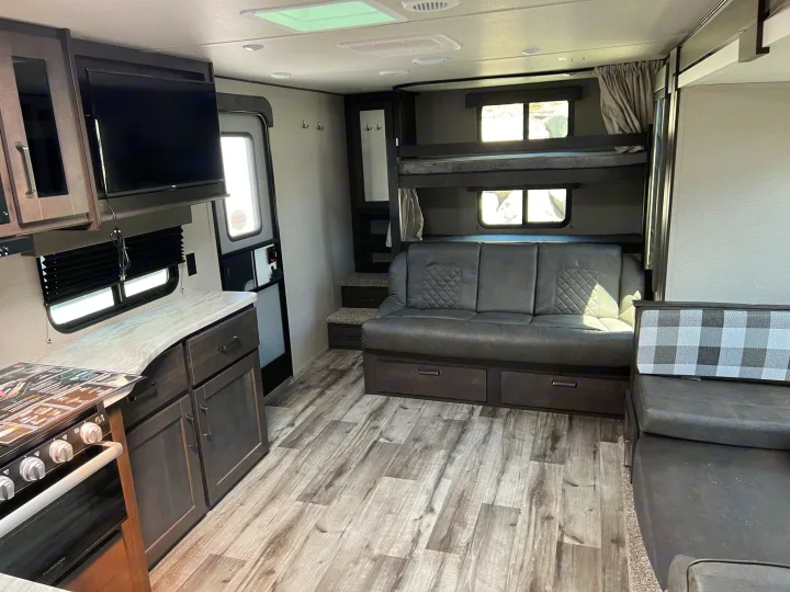 Spacious rv rental interior showing kitchen, living area with sofa, and bunk beds. Features light wood-look flooring.. Grand Design Transcend Xplor 2022