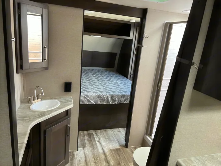 Inside a modern RV rental: bathroom vanity with sink on left, cozy bedroom visible through central doorway. Perfect for travels.. Grand Design Transcend Xplor 2022