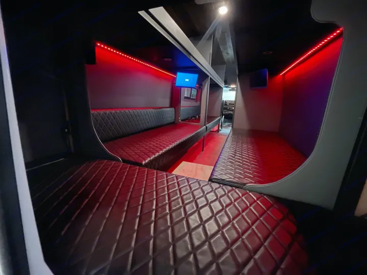 Inside this premium rv rental: A dark, modern interior with long, diamond-quilted benches, vibrant red LED strip lights, and entertainment screens.. Mercedes Sprinter Freight Liner 2020