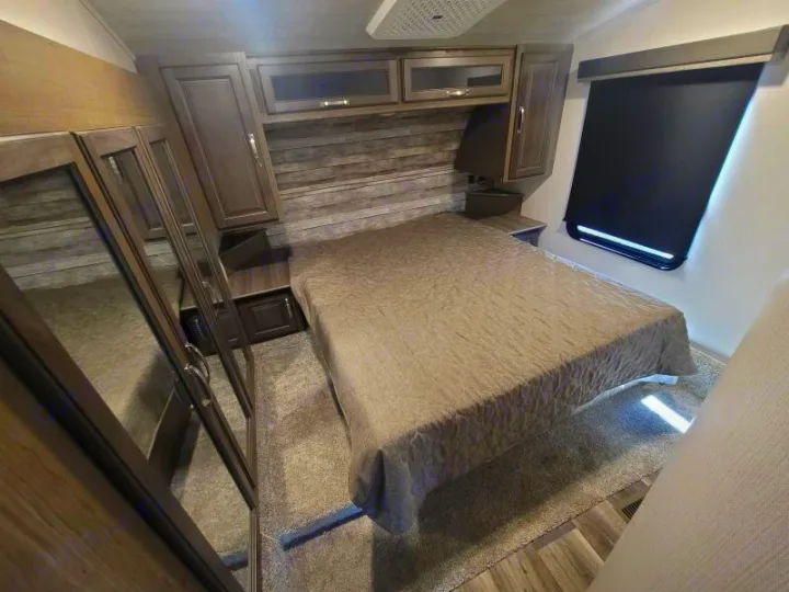 This RV rental bedroom features a bed, mirrored closet, overhead storage, and a window with a black shade.. Keystone Cougar 2022