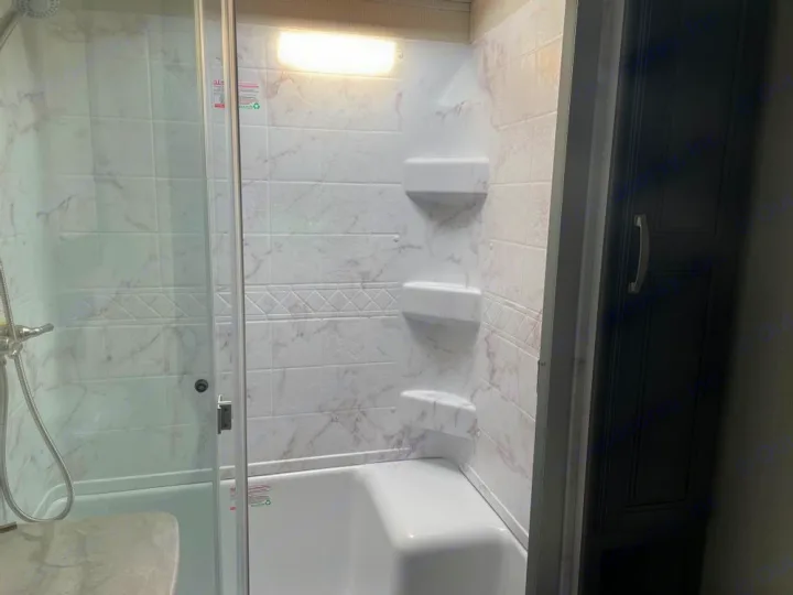 Clean RV rental bathroom with white shower/tub combo, glass door, and storage cabinet, ideal for travel.. Keystone Cougar 2022