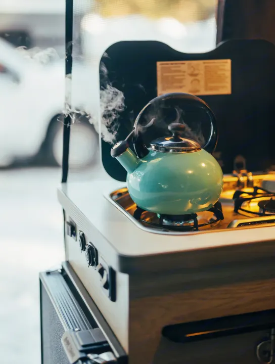 A teal kettle boils on a gas stove in an RV rental kitchen, with steam rising. Compact and convenient for travel.. Winnebago Solis 2022