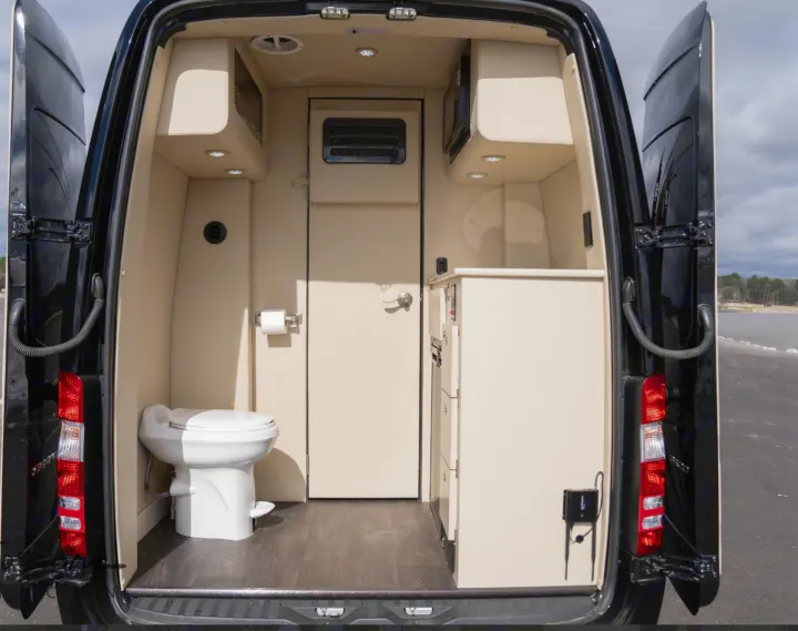 Inside a luxurious RV rental, showing the compact bathroom with a toilet and a small kitchen area with a microwave.. Midwest Automotive Designs Daycruiser 2019