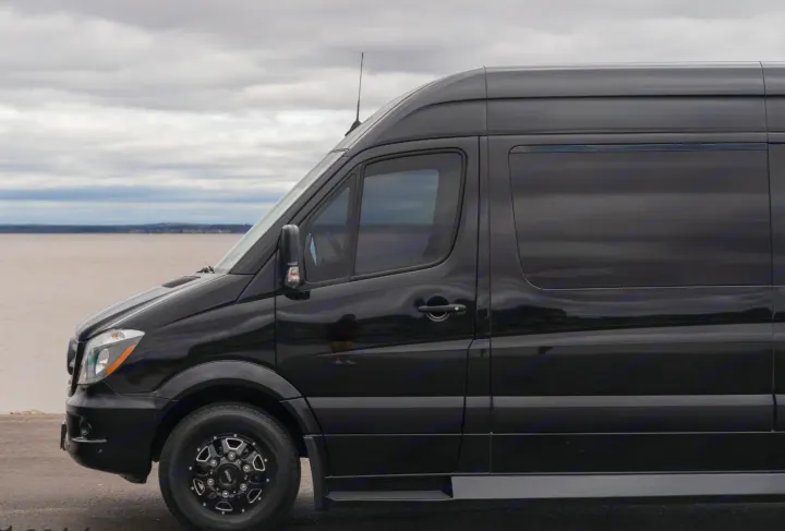 Sleek black luxury RV rental van parked by the water under a cloudy sky. Ready for your next road trip adventure.. Midwest Automotive Designs Daycruiser 2019