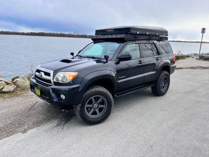 Black Toyota 4Runner with an iKamper rooftop tent parked by a lake. An ideal RV rental alternative for your next off-road adventure.. Toyota 4runner 2006