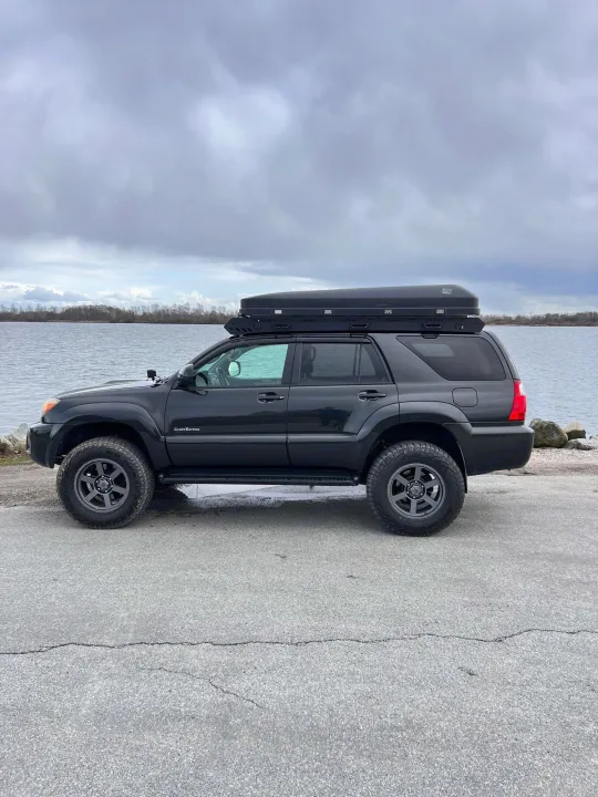 Explore with this adventure-ready SUV, a great alternative to an RV rental. Dark grey 4Runner with roof cargo box by a lake.. Toyota 4runner 2006