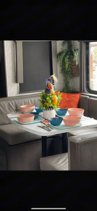 RV rental dinette set with vibrant pink and blue bowls on aqua plates. Features a fall scarecrow centerpiece and comfy booth seating.. Forest River Wildwood 2020