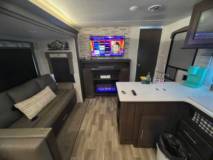 Cozy RV rental living space featuring a comfortable couch, TV, electric fireplace, and compact kitchen.. Forest River Wildwood 2020