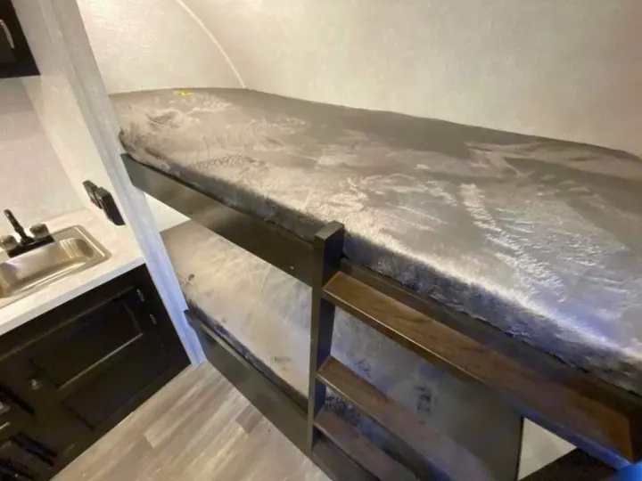 Cozy RV rental interior with bunk beds & compact kitchen counter featuring a sink. Perfect for travel adventures.. Braxton Creek Bushwhacker Plus 2021