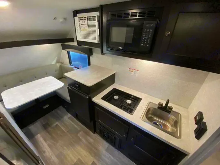 RV rental interior: compact kitchen (microwave, sink, stove) and a cozy dinette area for meals & seating.. Braxton Creek Bushwhacker Plus 2021