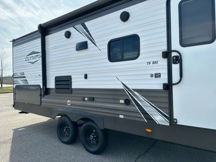 A detailed side view of an Olympia 26 BHS travel trailer, featuring white/grey siding and dual axles, great for rv rental.. Highland Ridge RV Olympia 2022