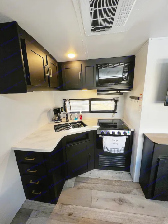 Modern RV rental kitchen with black cabinets, white counters, sink, and appliances. Ideal for your mobile adventures.. Keystone RV Springdale 2022